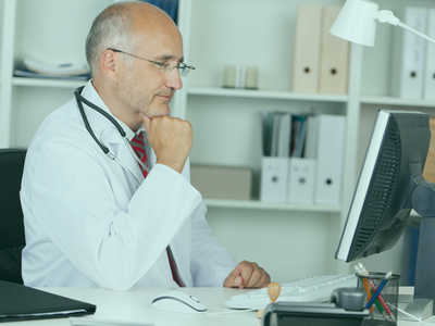 A physician sits at his desk in front of his computer